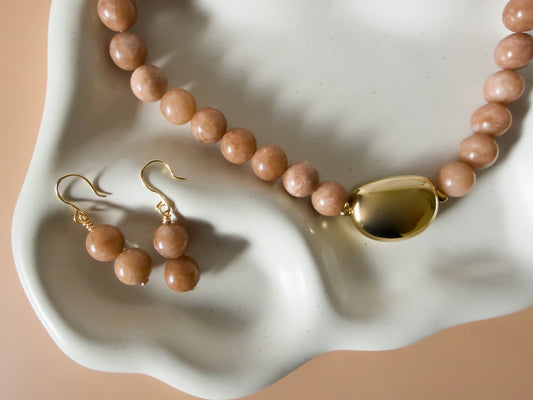 Necklace and earrings with peach-colored beads and gold accents on a white dish.
