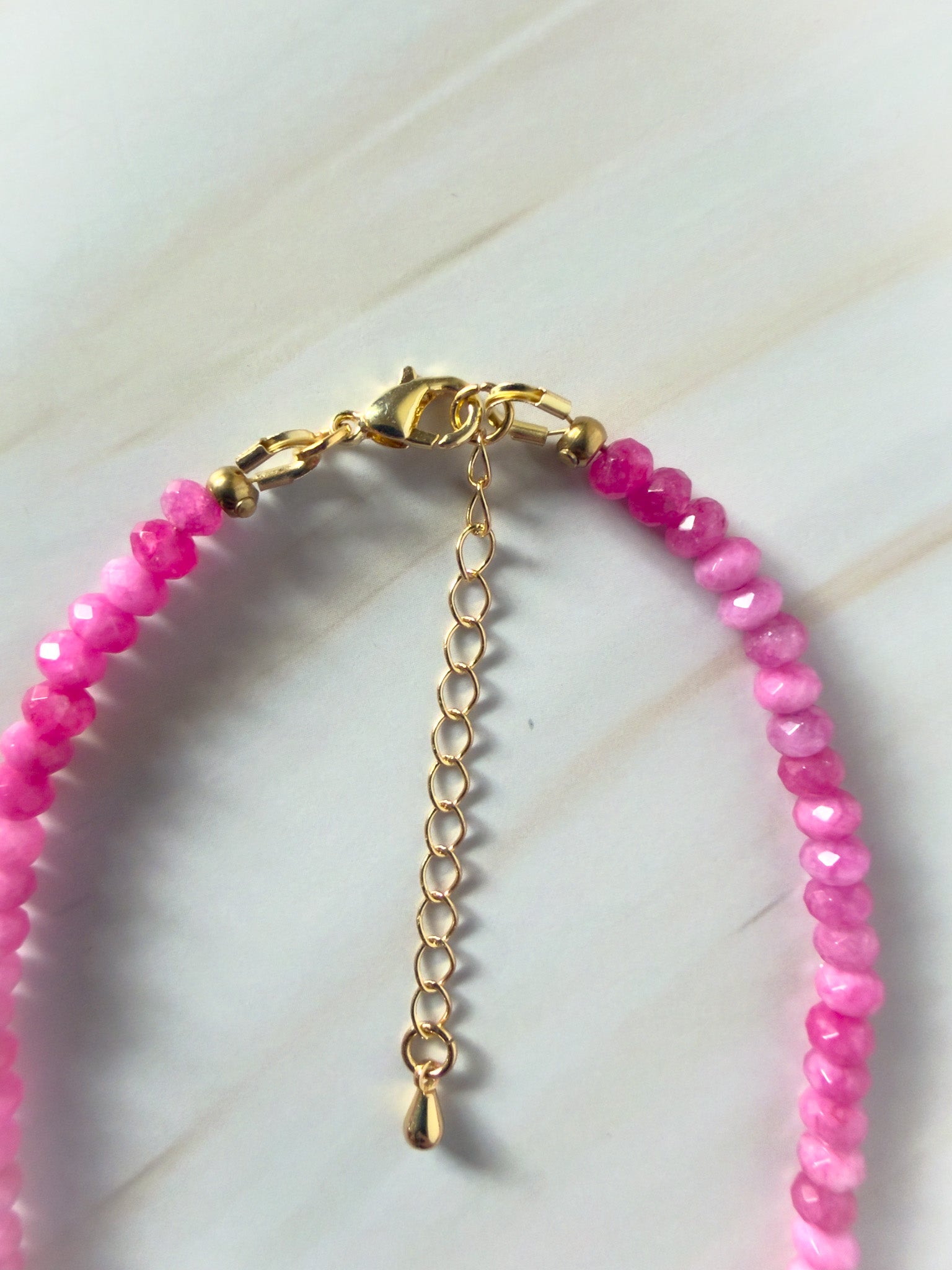 Pink beaded necklace with gold clasp on a light background