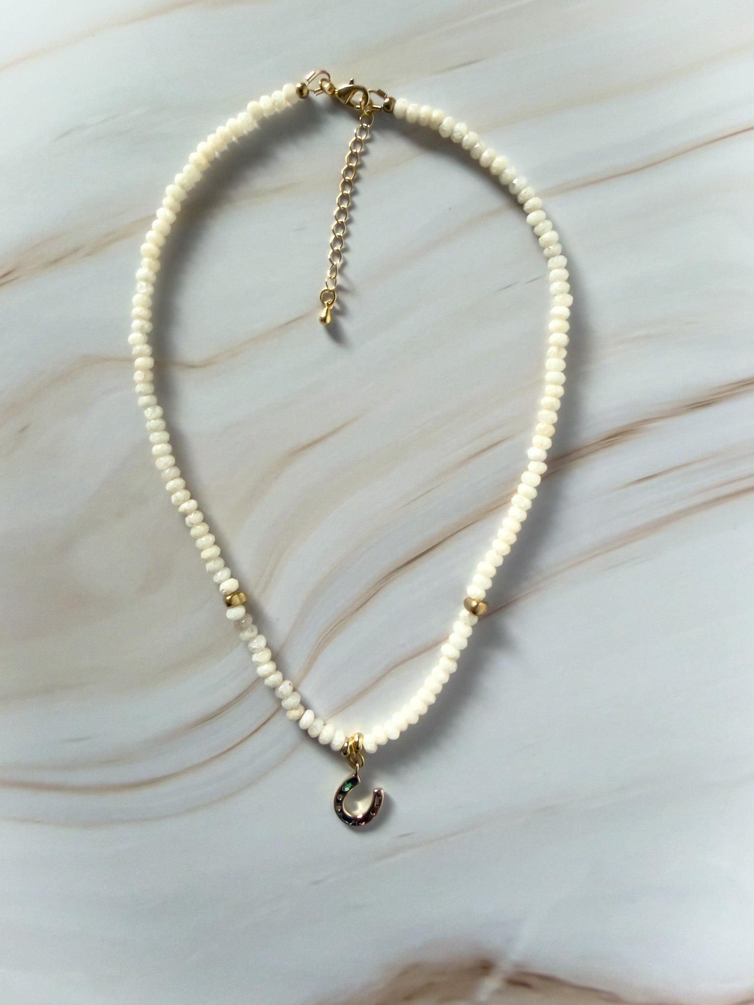 Necklace with white jade beads and a small charm on a marble surface