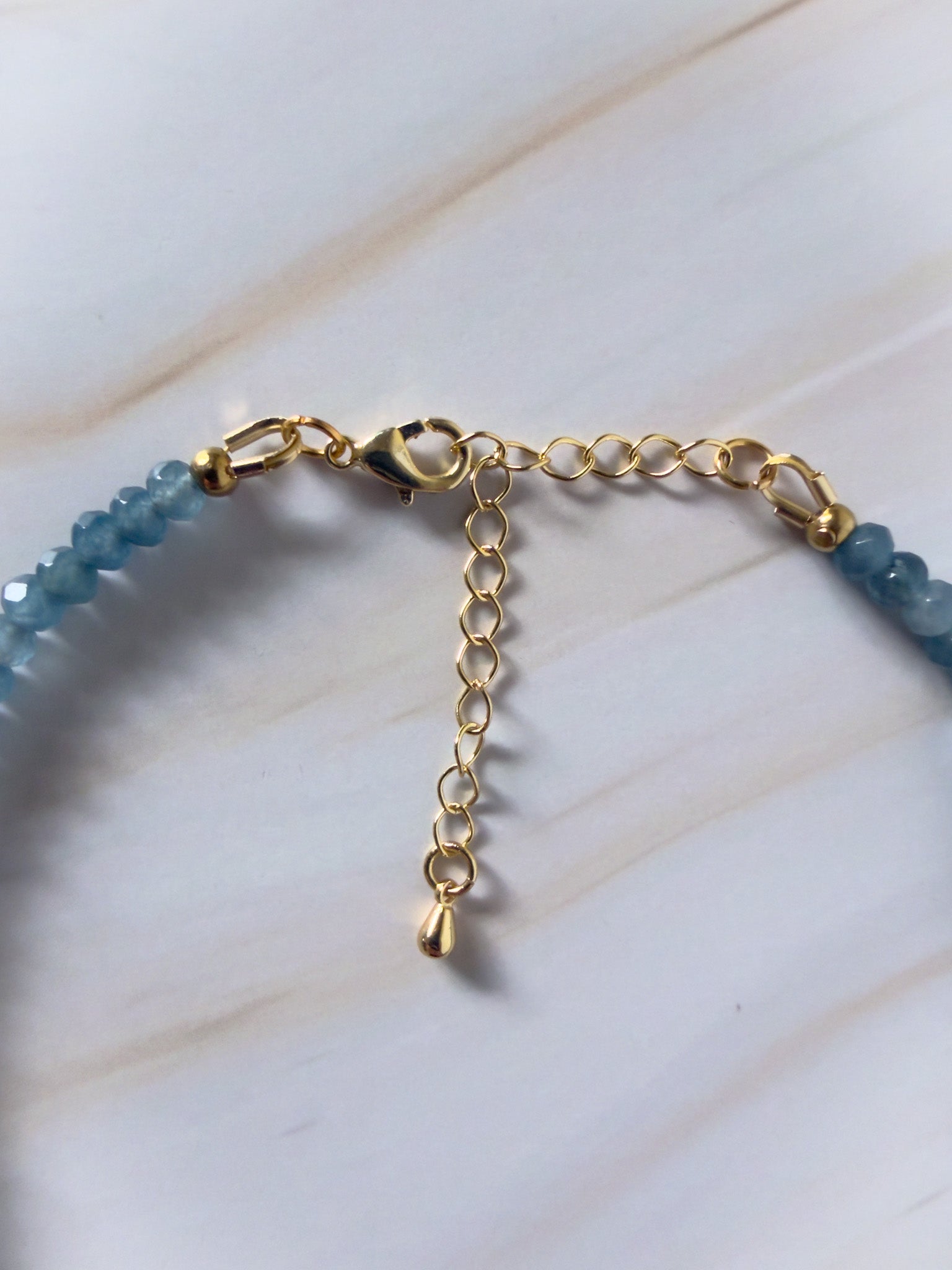Gold necklace with blue beads on a white background