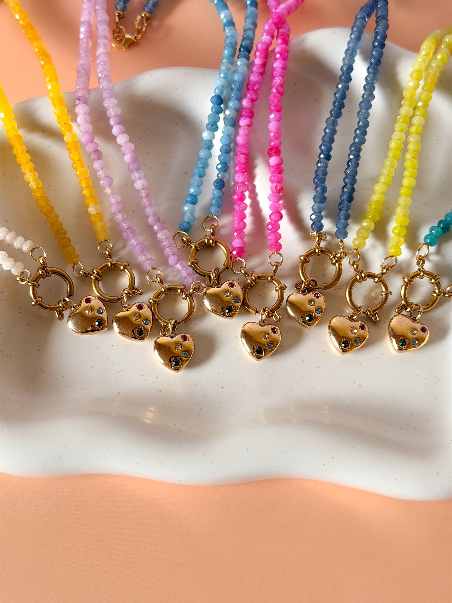 Colorful beaded necklaces with gold heart-shaped pendants on a white surface.