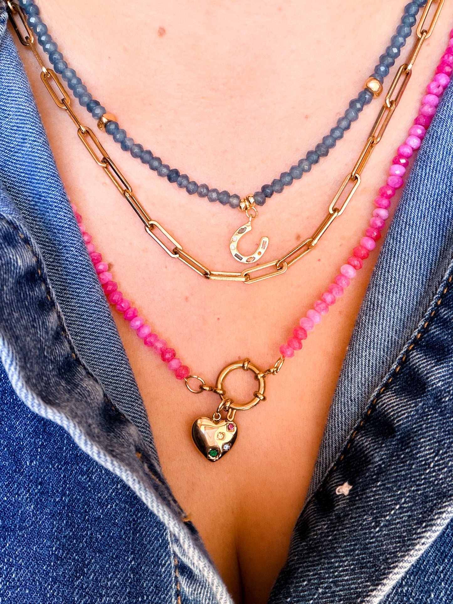 Necklace with pink beads and gold clasp on a person wearing denim clothing.