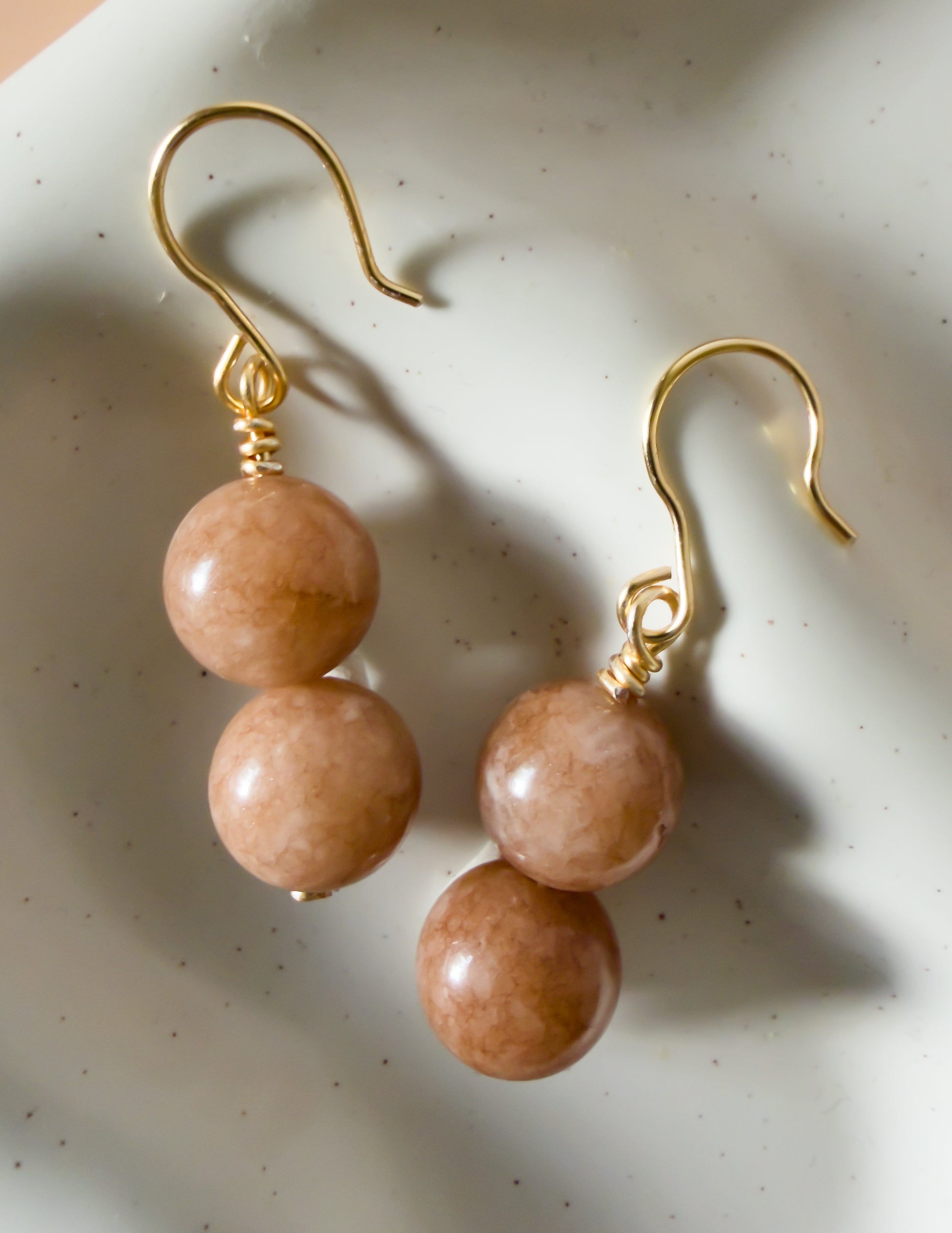 Pair of handmade gold earrings with gemstone beads on a textured white surface