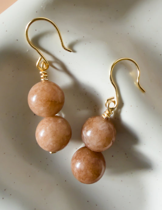 Pair of handmade gold earrings with gemstone beads on a textured white surface