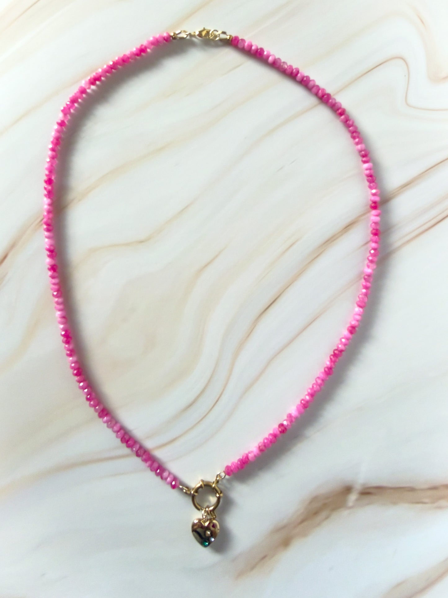 Pink beaded necklace with gold heart charm on a marble surface