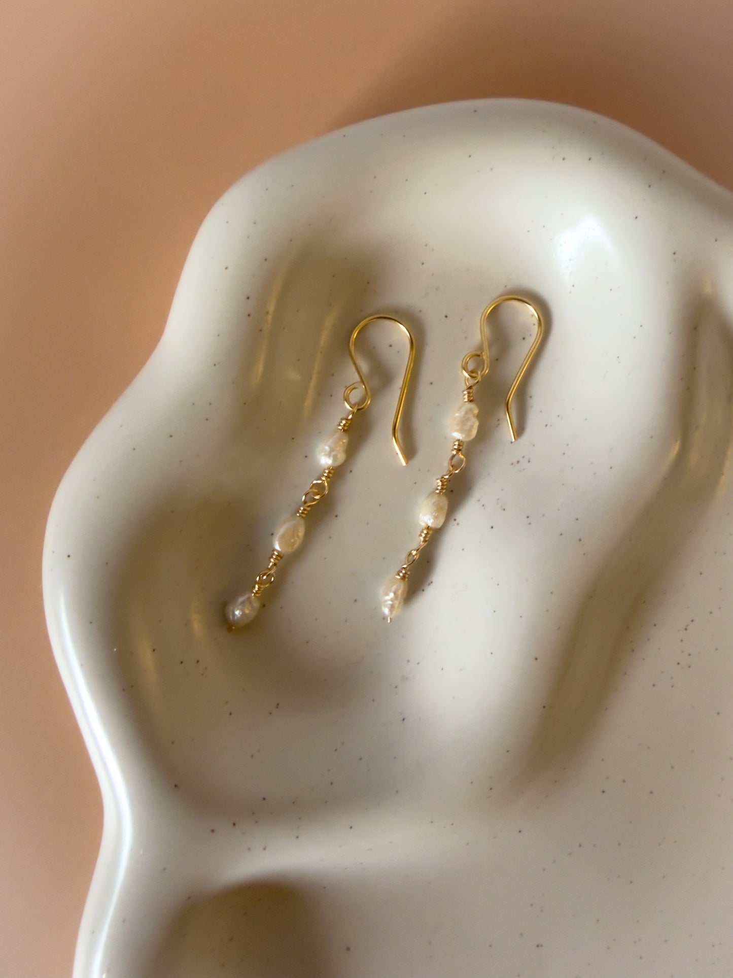 Gold earrings with pearls on a textured white surface