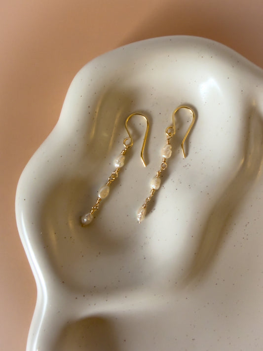 Gold earrings with pearls on a textured white surface