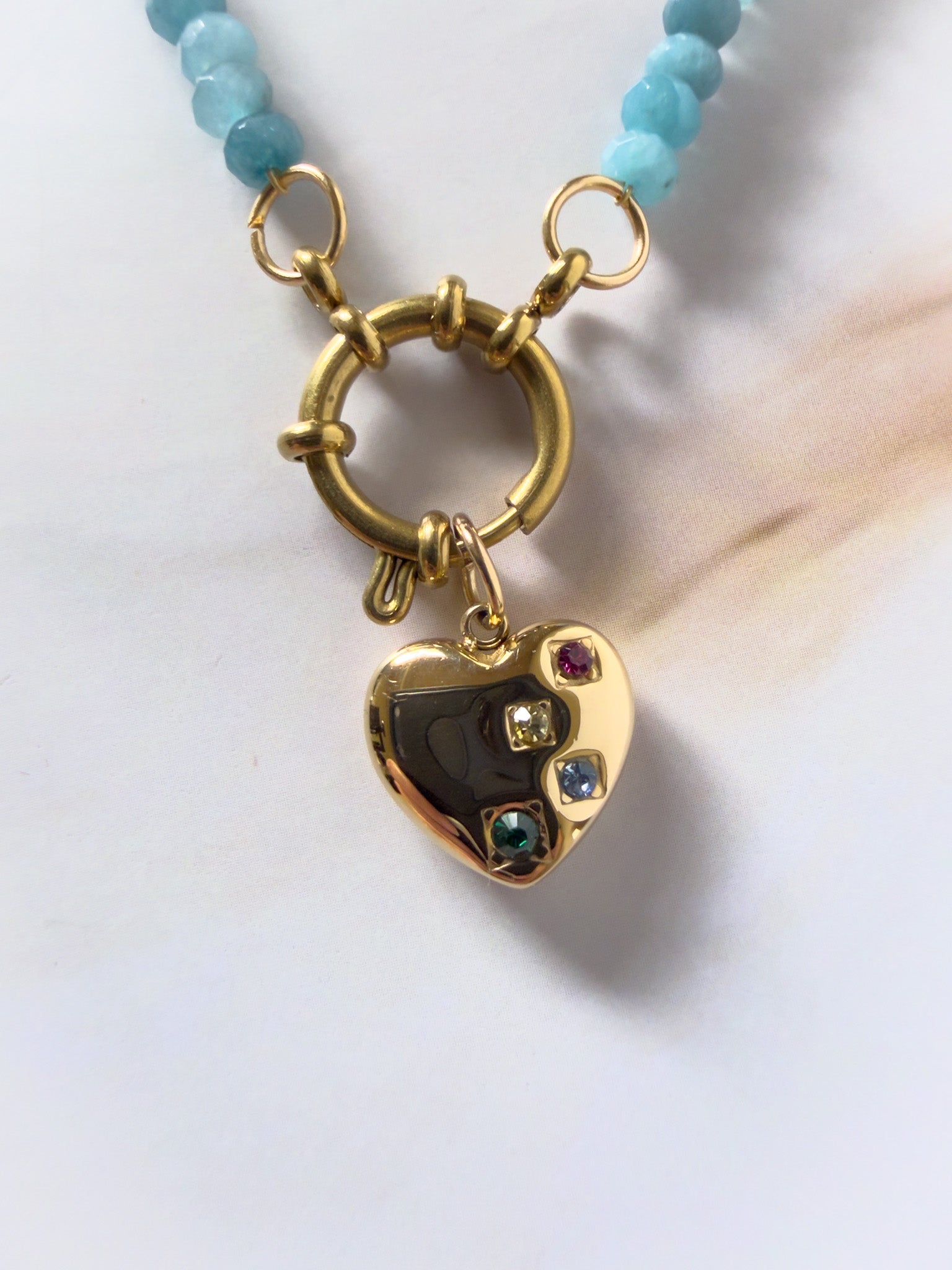 Gold necklace with a heart-shaped pendant featuring gemstones on a white background