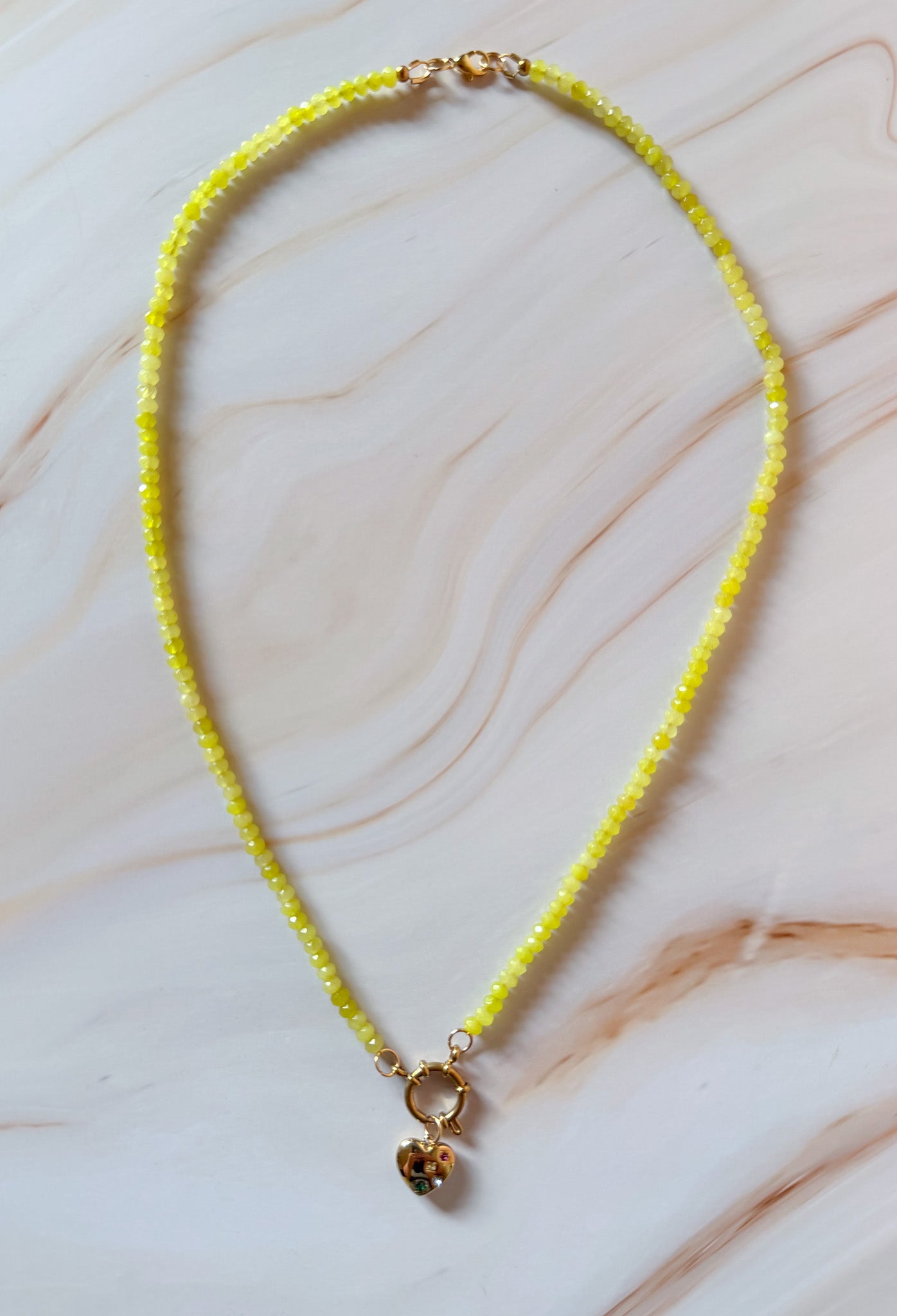Necklace with yellow beads and a small pendant on a marble surface