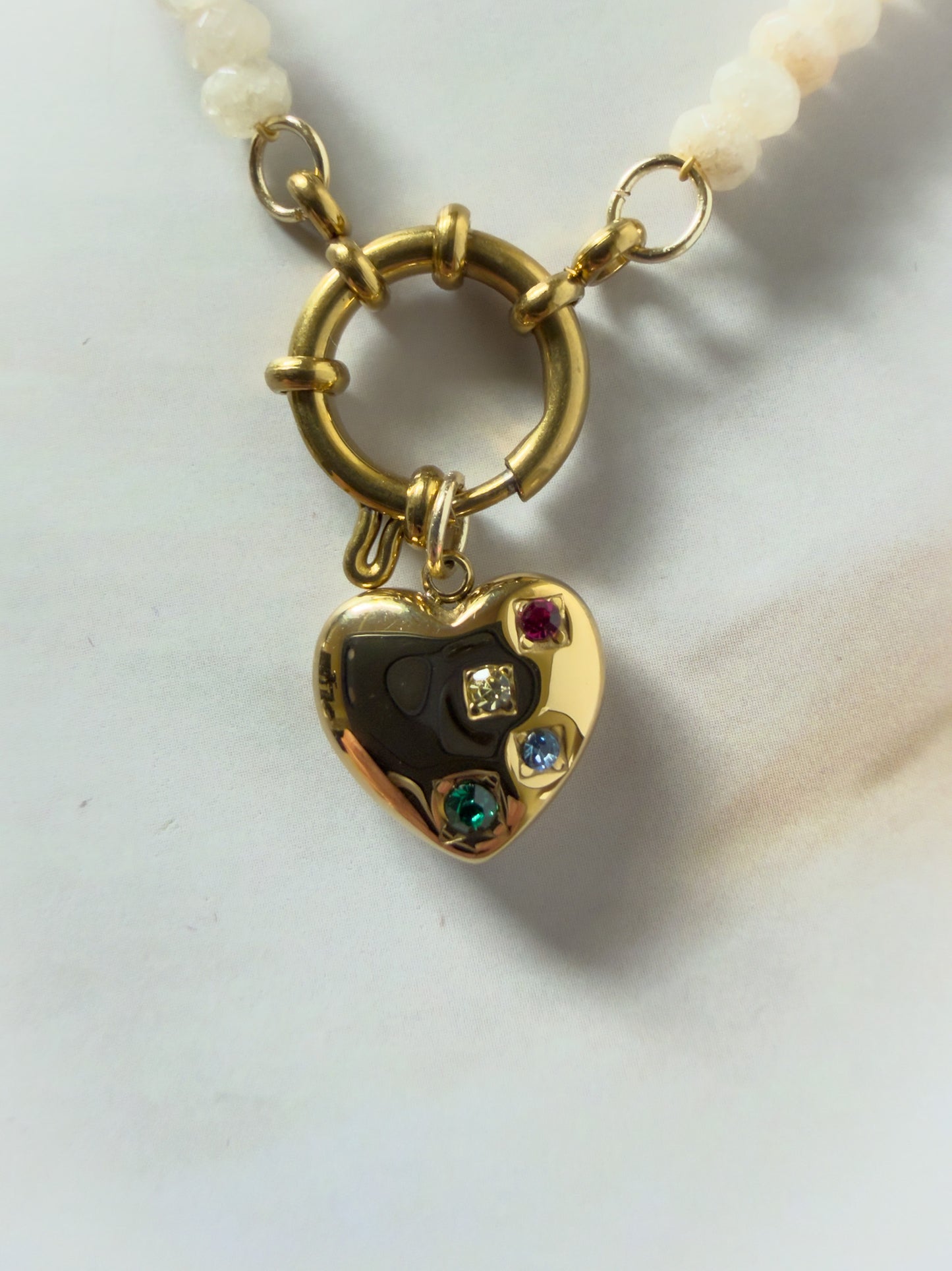 Gold heart-shaped pendant with colored stones on a white background