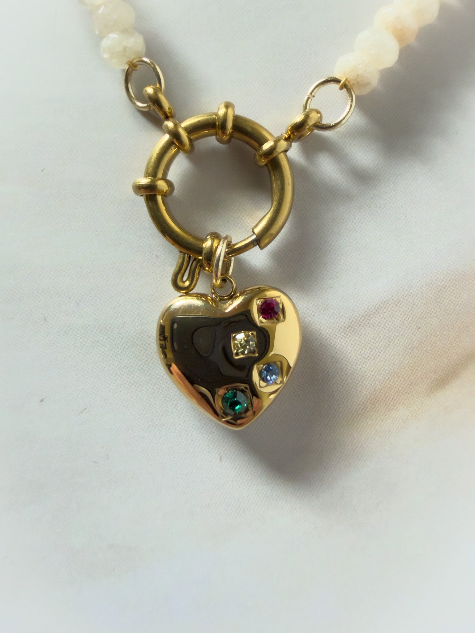 Gold heart-shaped pendant with colored stones on a white background