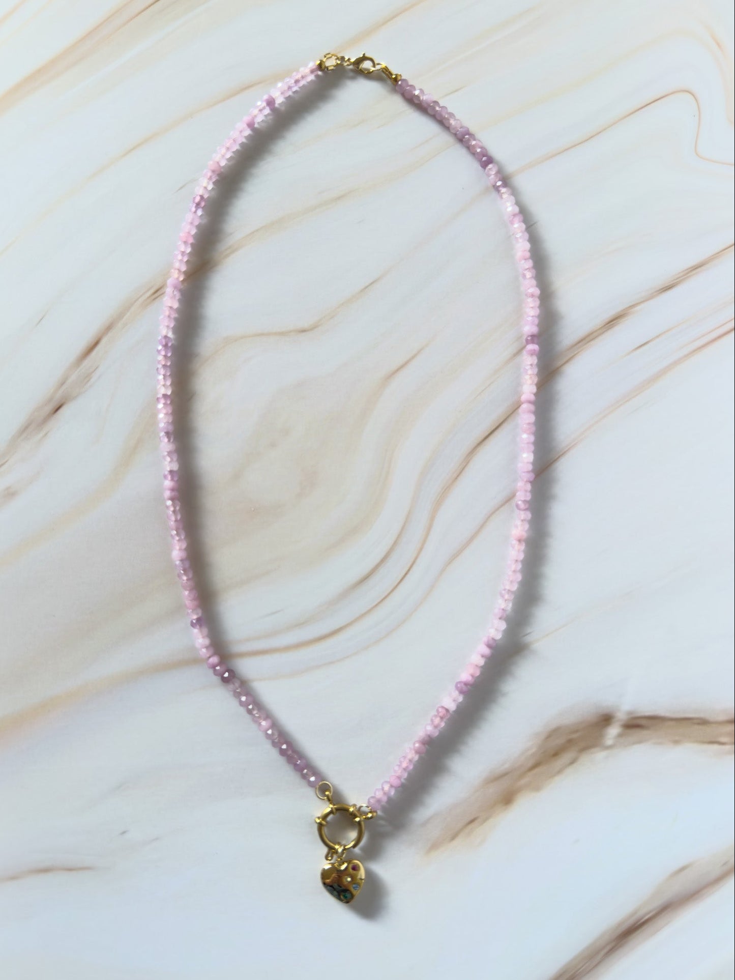Lavender beaded necklace with a gold heart pendant on a marble surface
