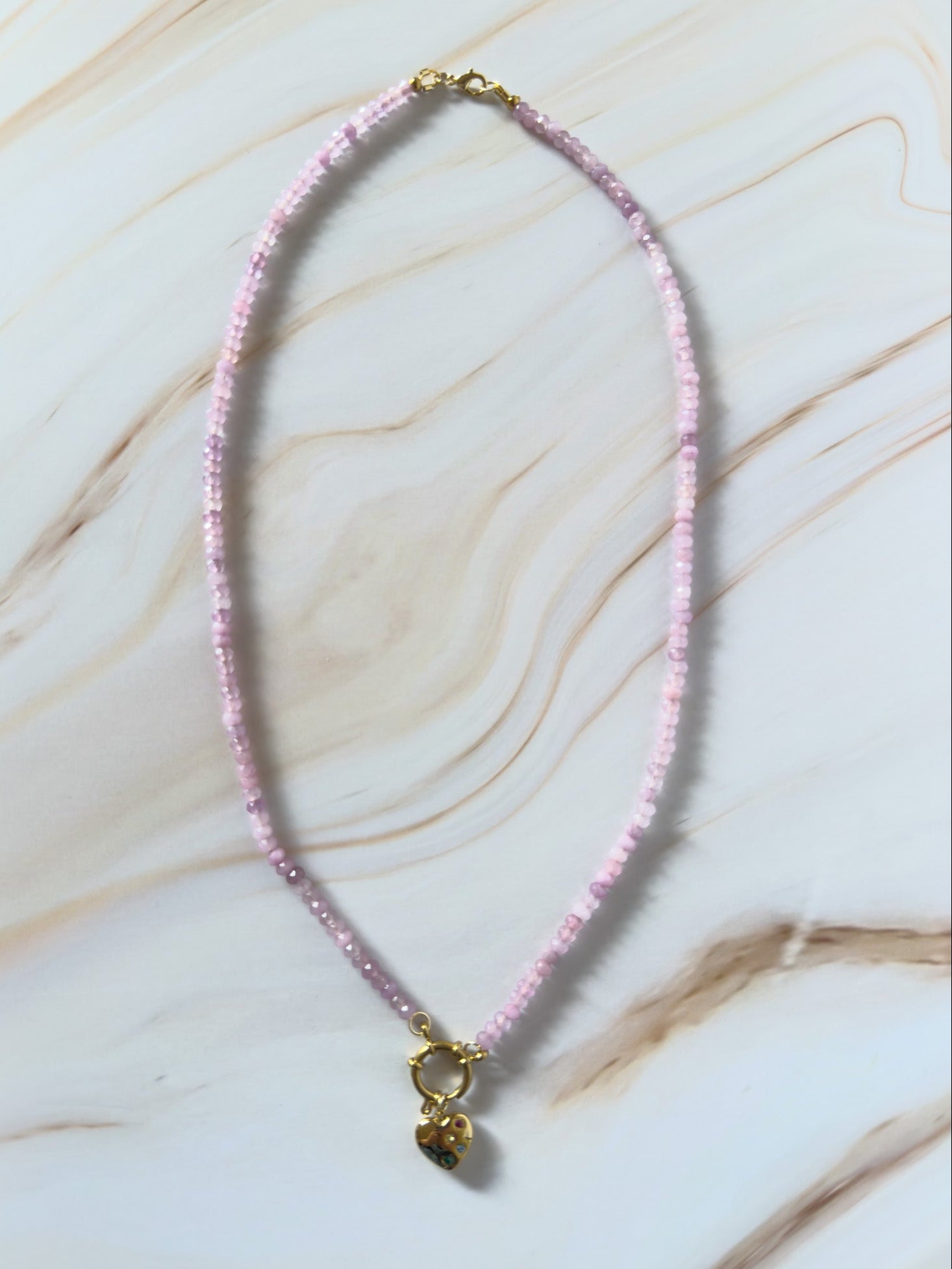 Lavender beaded necklace with a gold heart pendant on a marble surface
