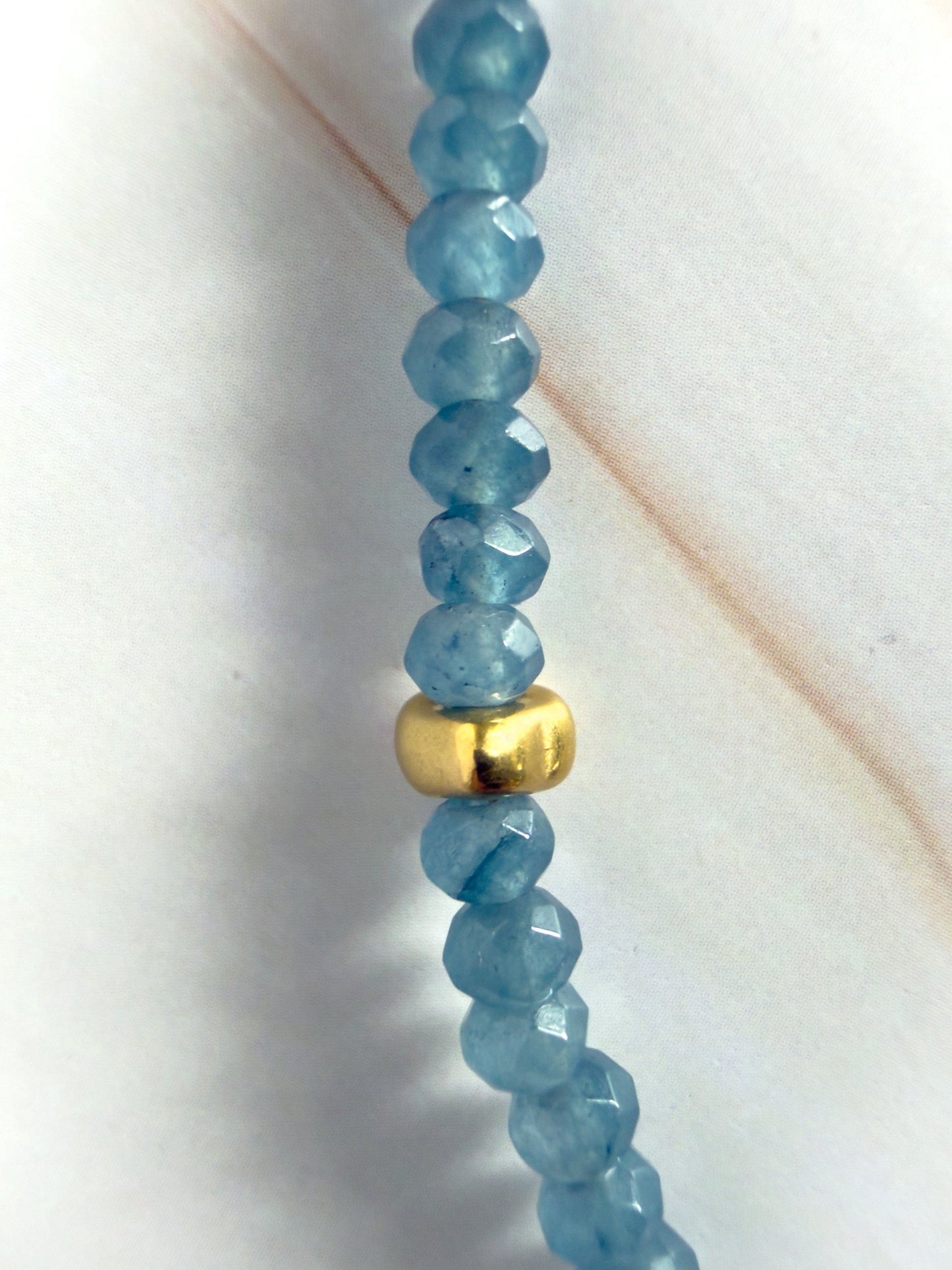 Blue beaded necklace with a gold accent on a white background