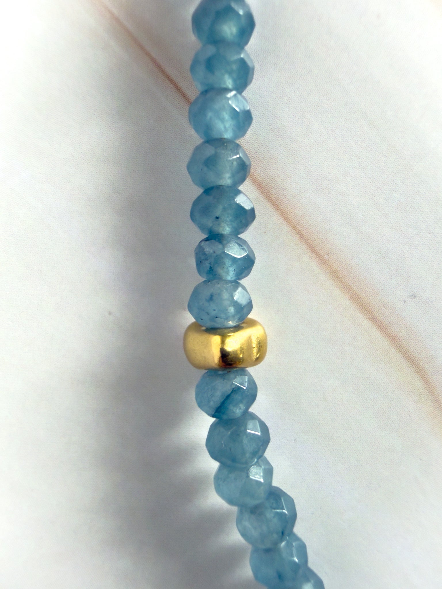 Blue beaded necklace with a gold accent on a white background