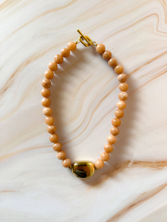 Beaded stone necklace with gold clasp on a marble surface