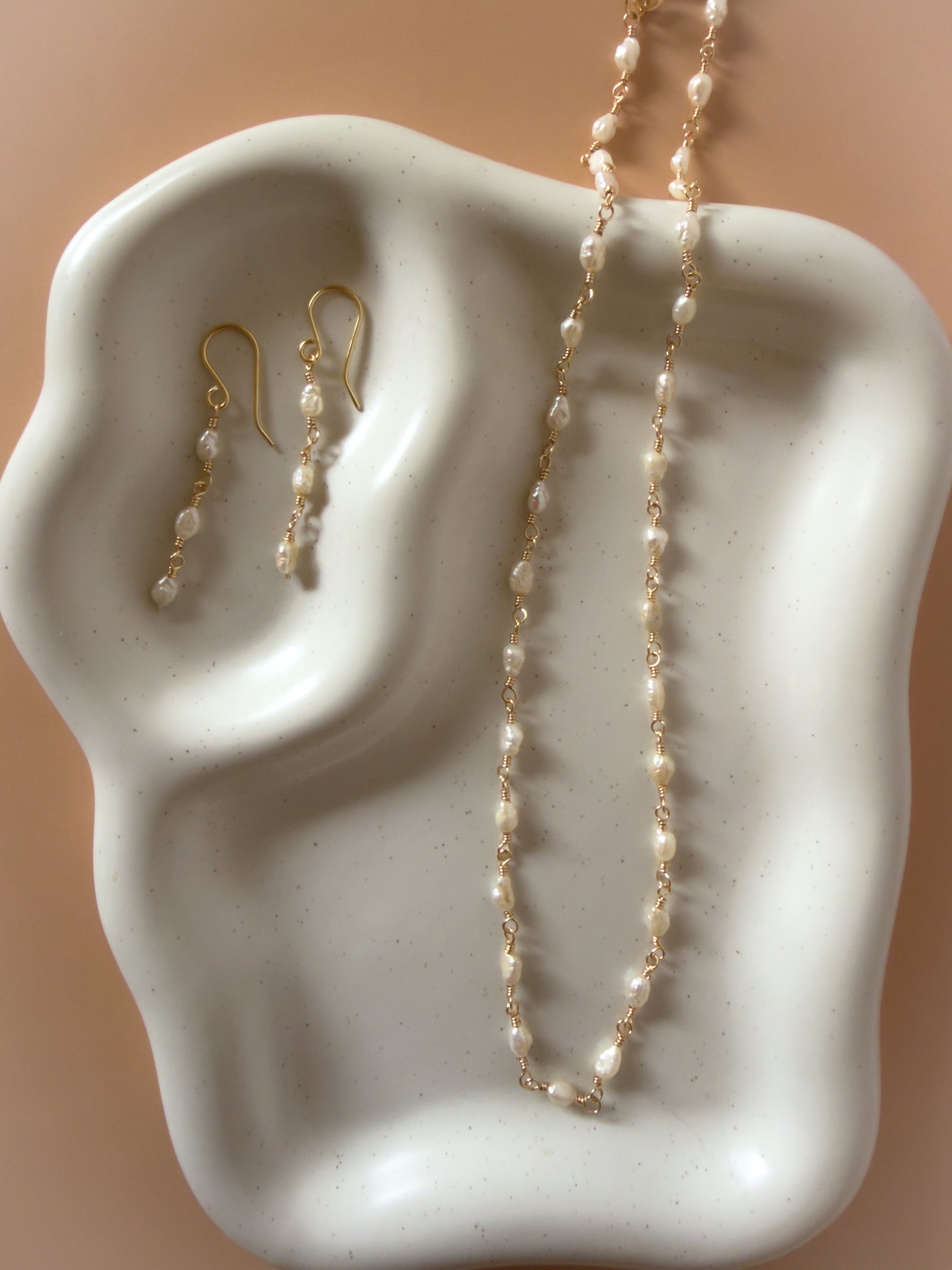 Pearl necklace and earrings on a white ceramic ear model with a beige background